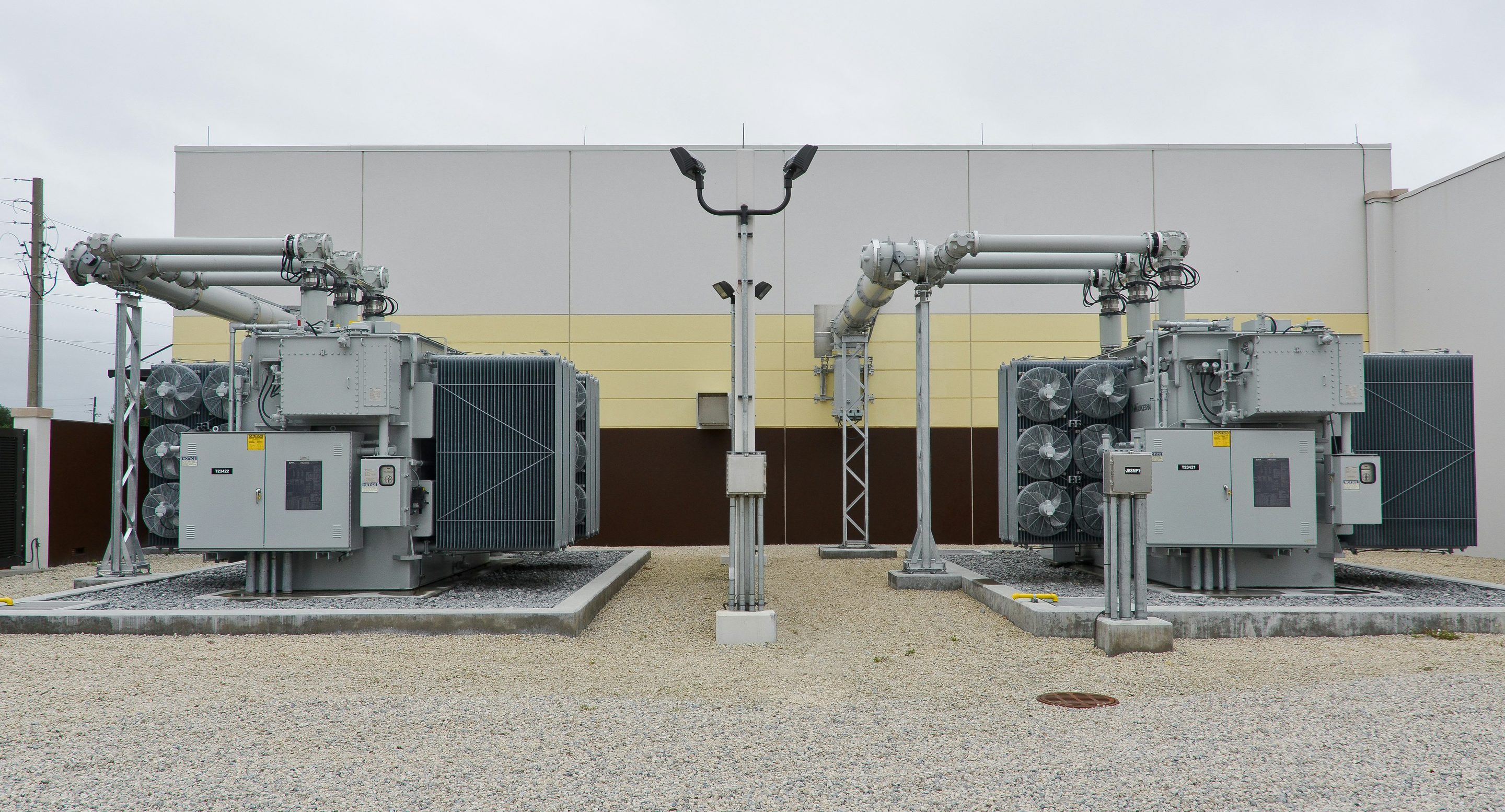 Two power transformers with radiator banks and overhead conductors in a substation yard, under flat overcast light