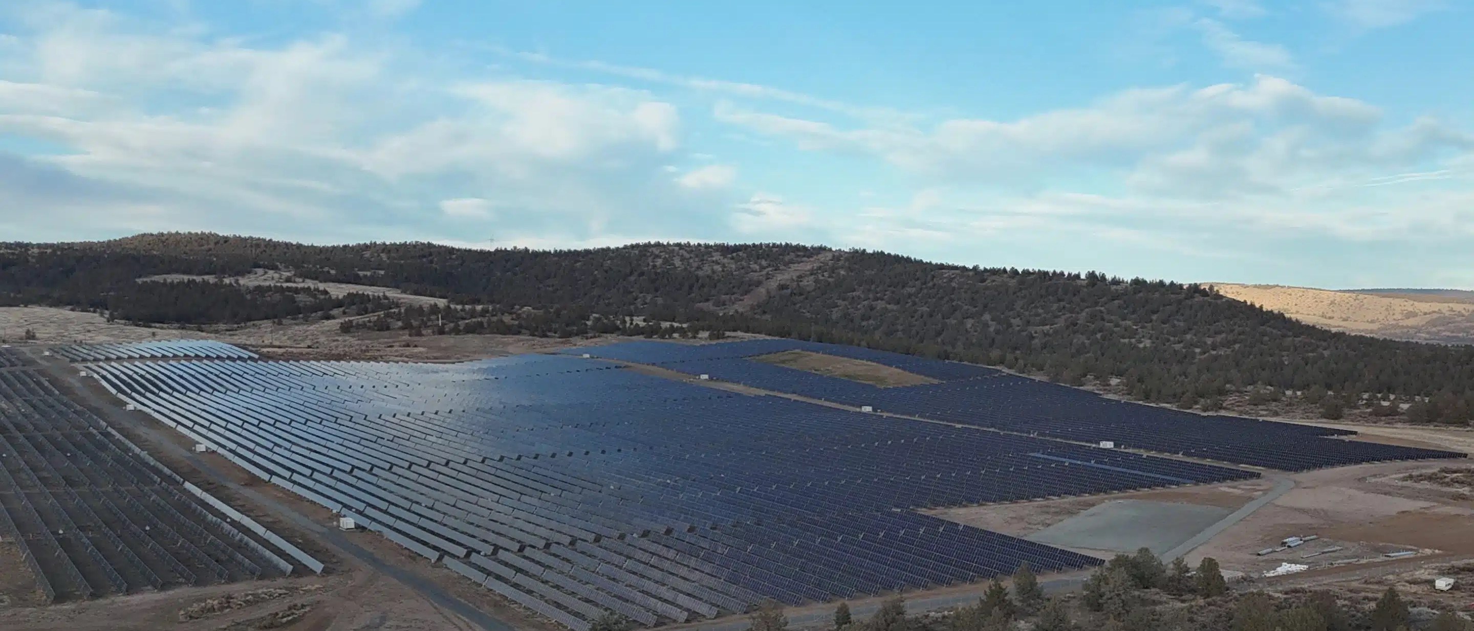 Utility-scale solar array on high desert land, with forested hills behind